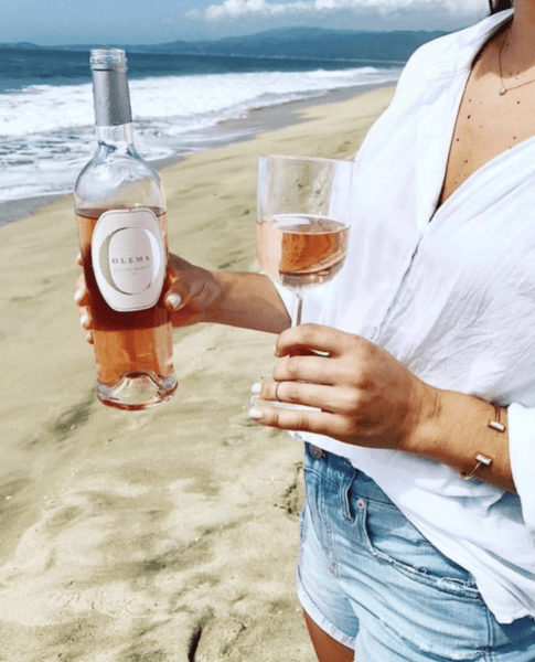 Woman holding a glass and bottle of Olema Rosé on the beach